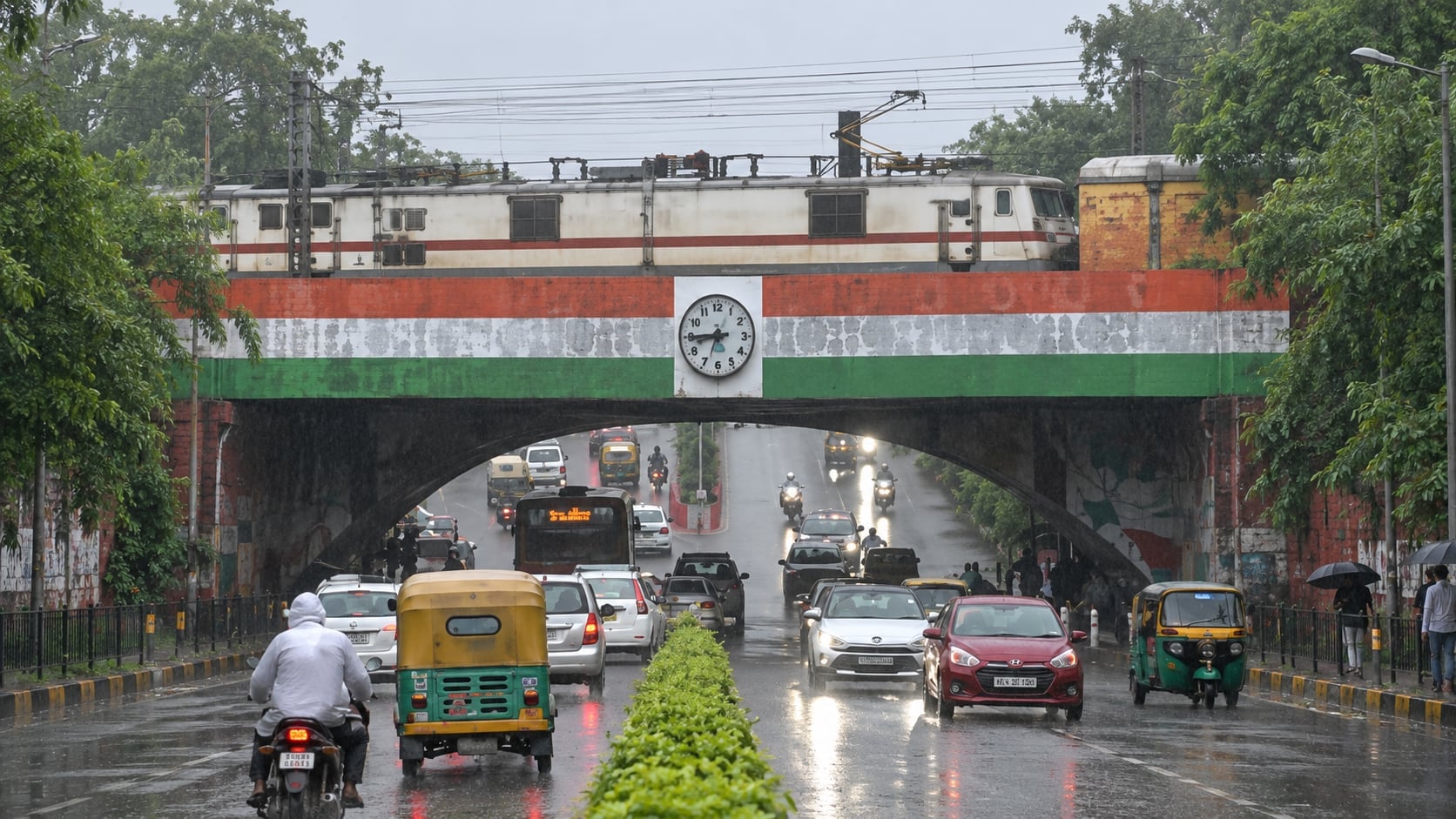 User-supplied after view identified as the Minto Bridge underpass, Delhi, with traffic moving through in rain and a locomotive crossing above